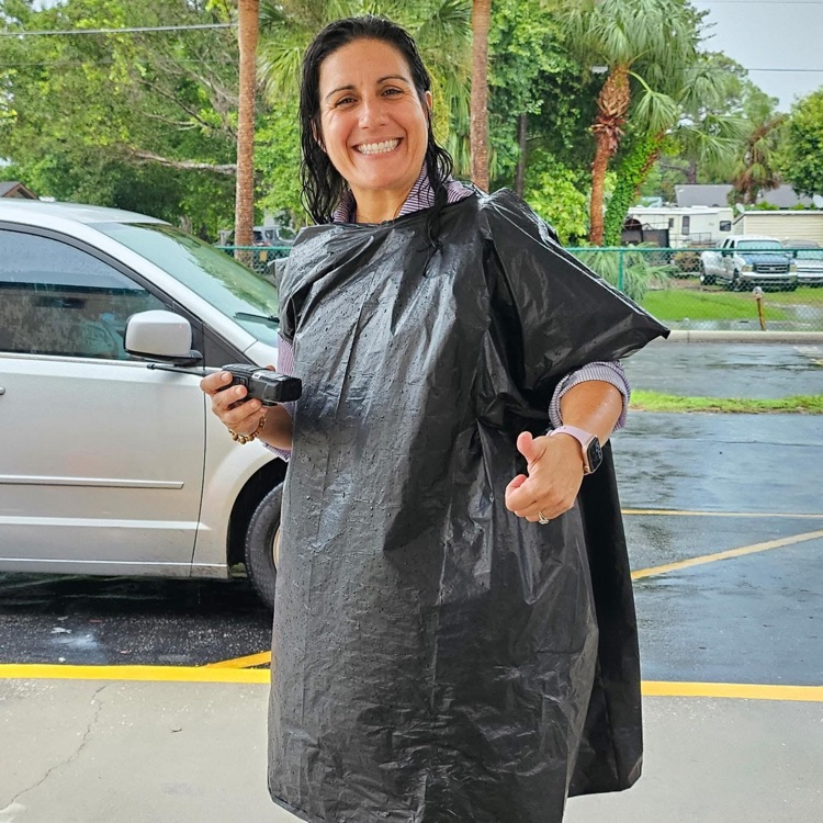 A smiling woman in a black rain poncho during dismissal at a school in the rain