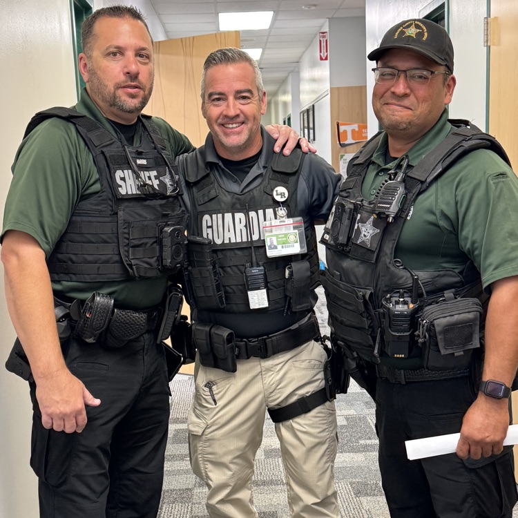 Two deputy SROs and a school guardian stand inside the front office