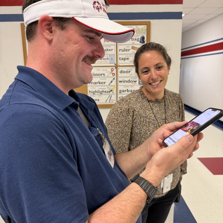 A man watches a video on a cell phone, while his supervisor smiles and watches on