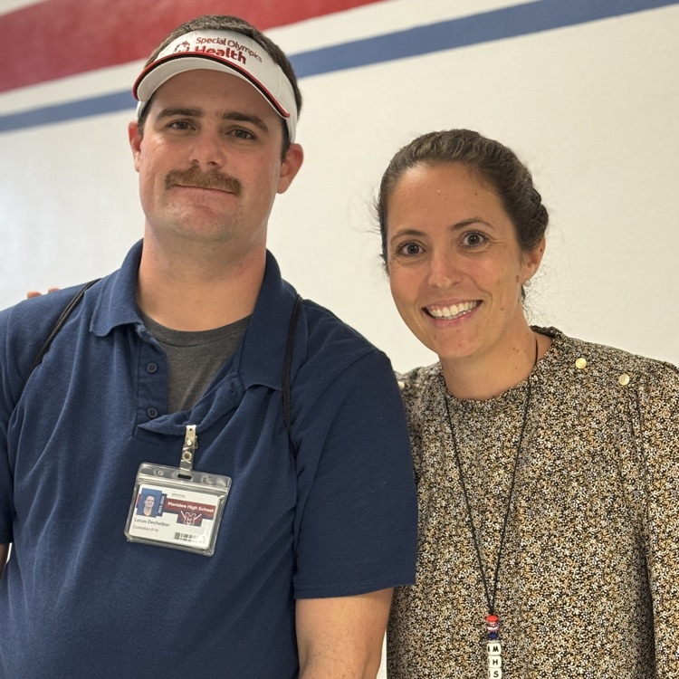 To colleagues stand shoulder to shoulder smiling for a photo
