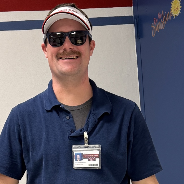 A man wearing sunglasses, smiling, and wearing a blue shirt