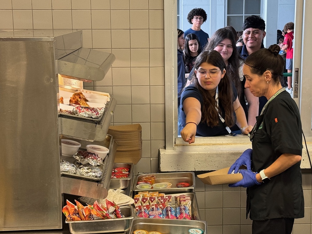 a student points to trays of food in a food service grab and go window.