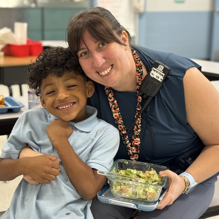 An educator sits with a student at lunch