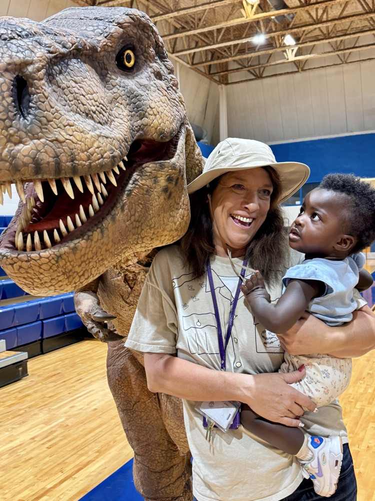 A teacher holding a toddler next to in the animatronic dinosaur