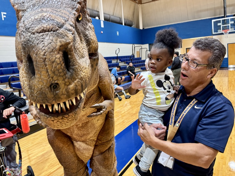 Another teacher holding a toddler next to an animatronic dinosaur