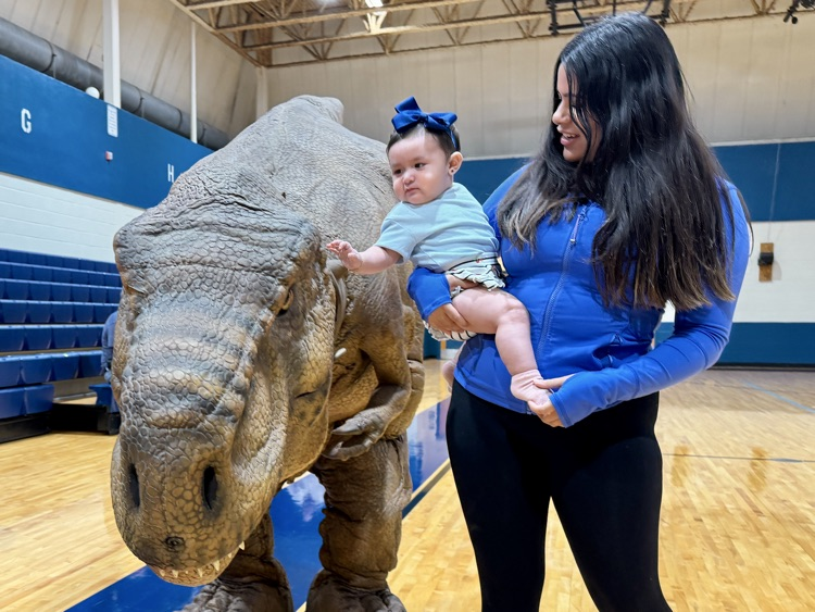 A staff member holding a toddler next to an animatronic dinosaur
