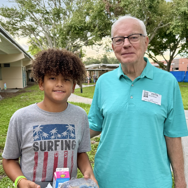 A man and a boy smile while standing in a school courtyard.