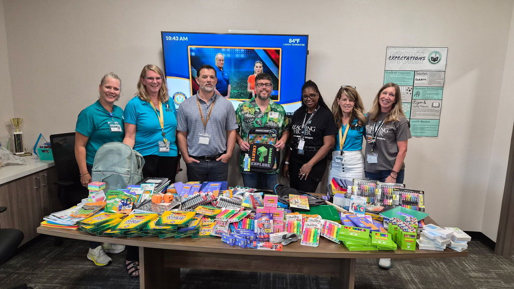 A group of adults standing in front of a table covered in brand new school supplies.