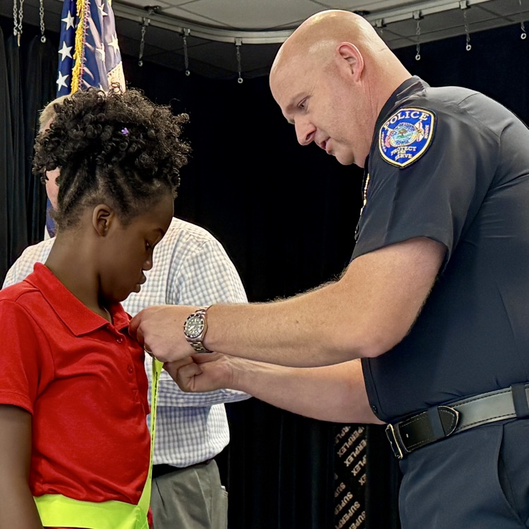 The assistant, chief of police places, a pin on the belt of a safety patrol