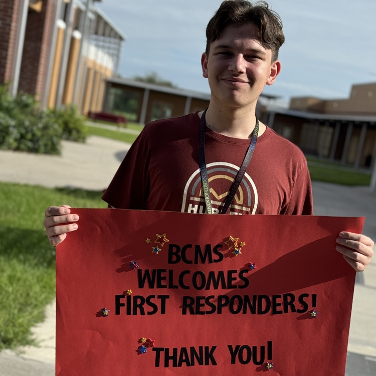 A boy holds a sign welcoming, first responders to his school