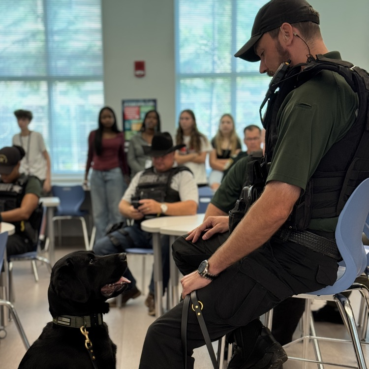 A sheriff’s deputy and his canine partner in the media center with students watching on