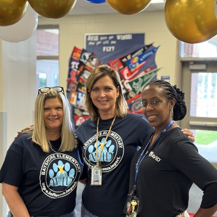 Three school leaders stand smiling in a school. 
