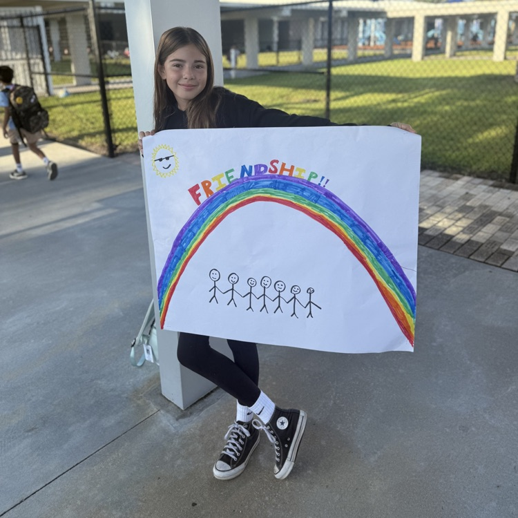 A young girl with black Converse sneakers holds a sign with a rainbow on it that says the word friendship