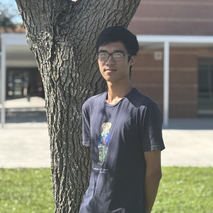 A young man stands next to an oak tree on his high school campus