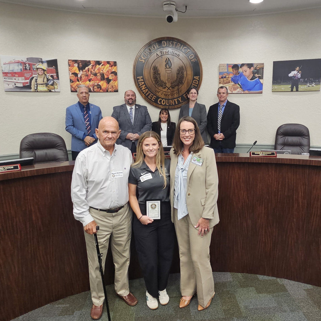 School board members stand with a valued employee during a meeting.