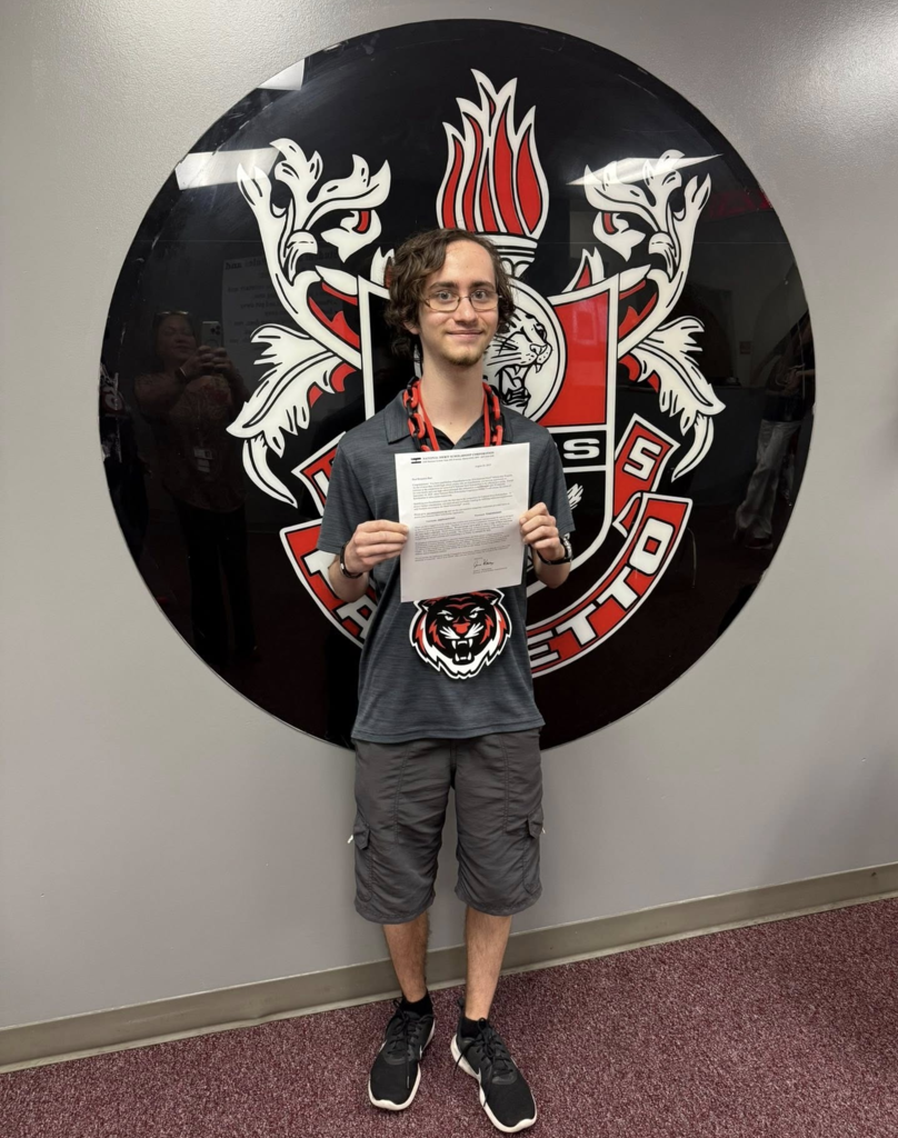 A teen stands in front of his school logo for Palmetto High.