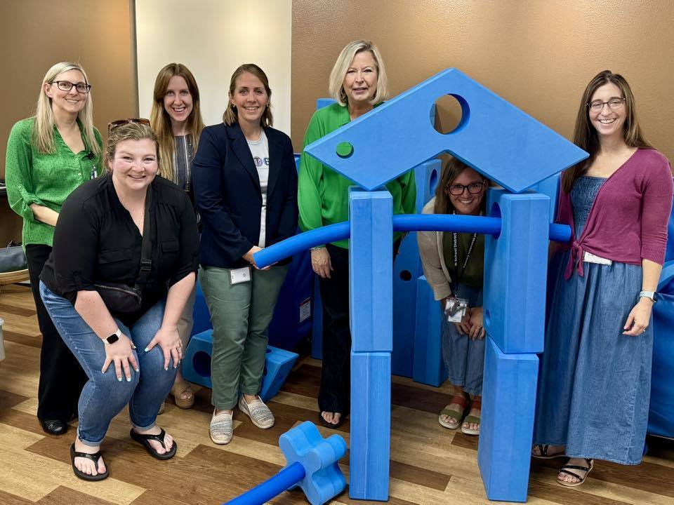 A group of education professionals smile while standing among giant blue foam pieces.