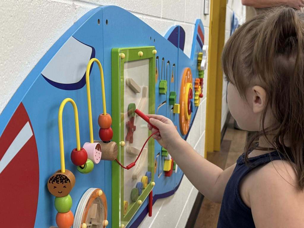 A young girl intently playing with an interactive toy hanging from a wall.