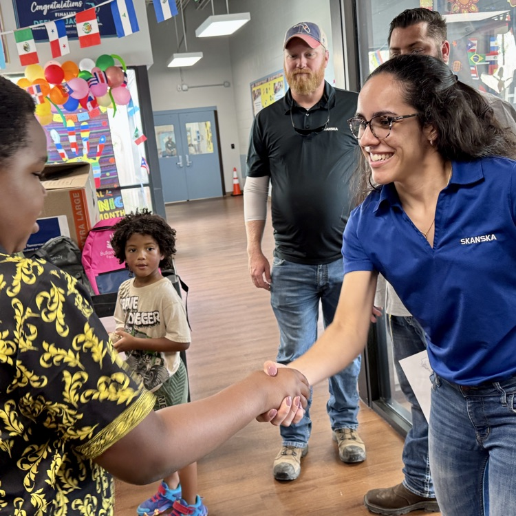 A young student shakes a woman’s hand after she and her teammates deliver a donation to his school
