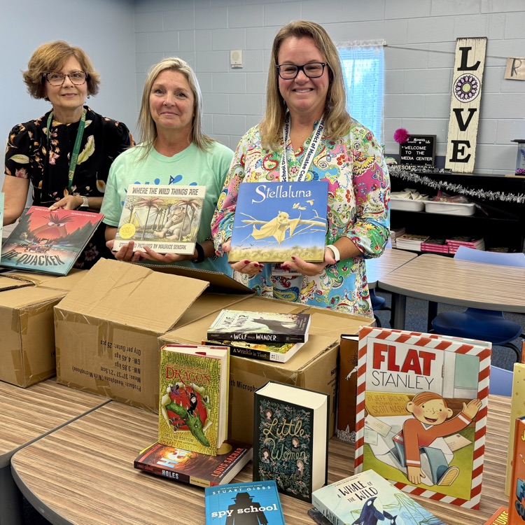 Three women standing with boxes filled with brand new books for a school