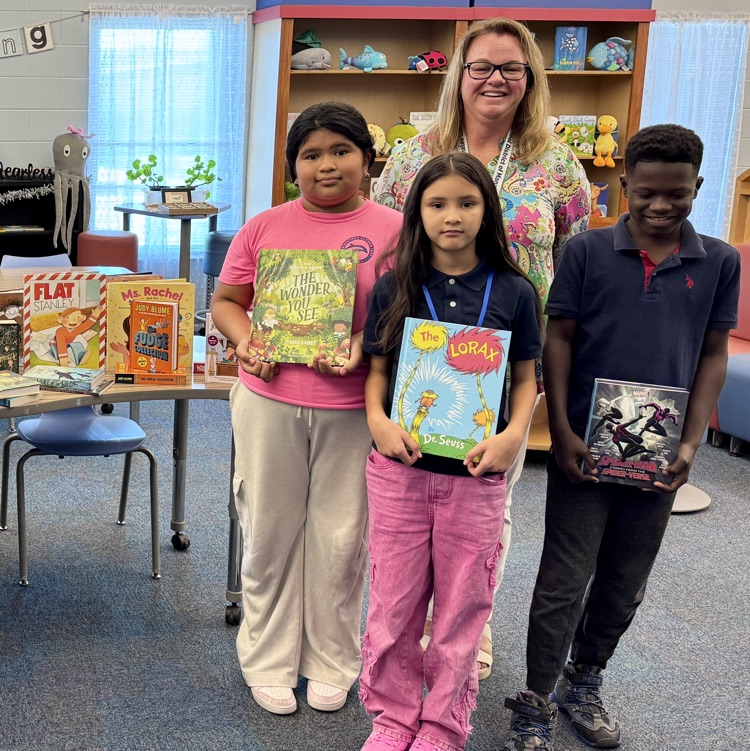 A school principal with students holding books and smiling