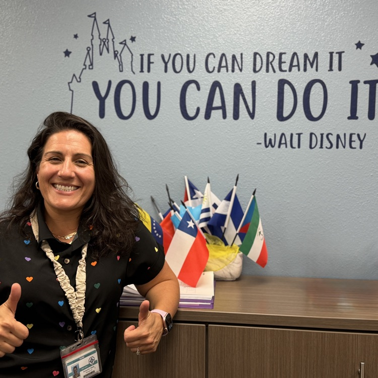 A school principal, giving the thumbs up in front of a Walt Disney quote posted on the wall