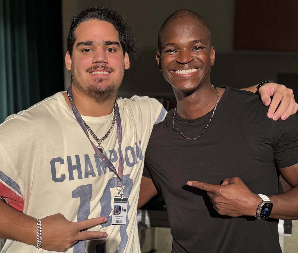 A young man wearing a shirt that reads "Champion" standing with Darian Sanders, an author, actor, and speaker.