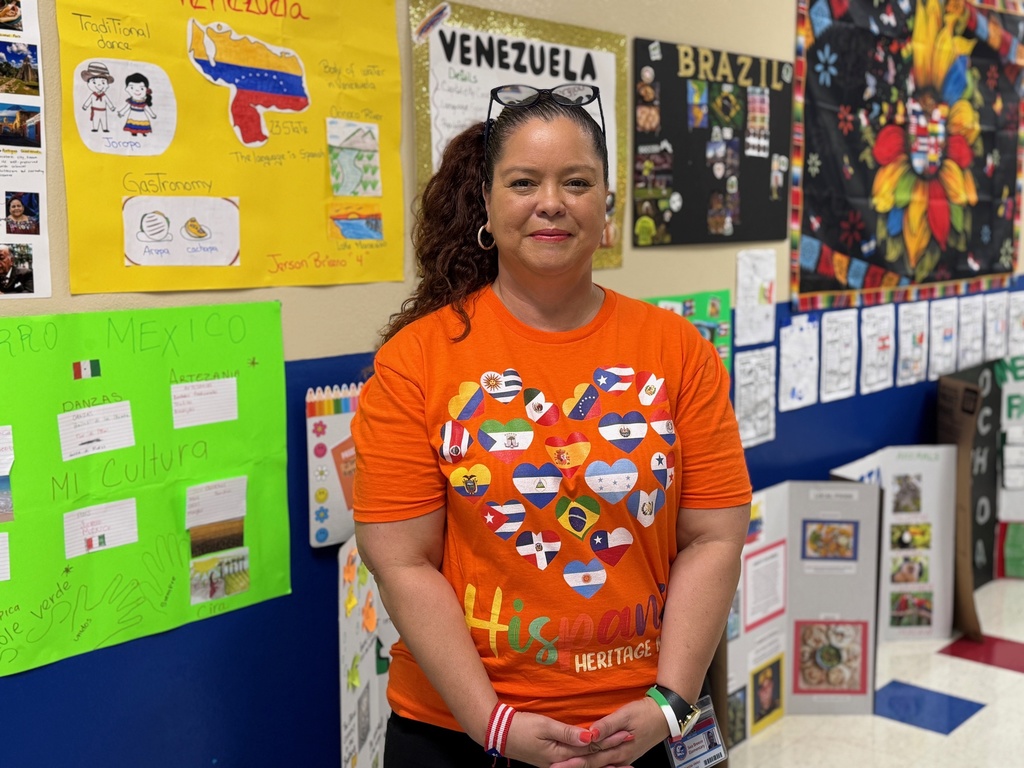A teacher wearing a bright orange tshirt which reads, "Hispanic Heritage Month"