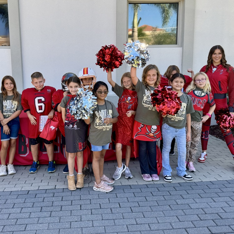 A buck cheerleader with students from Myakka City who are holding pom-poms