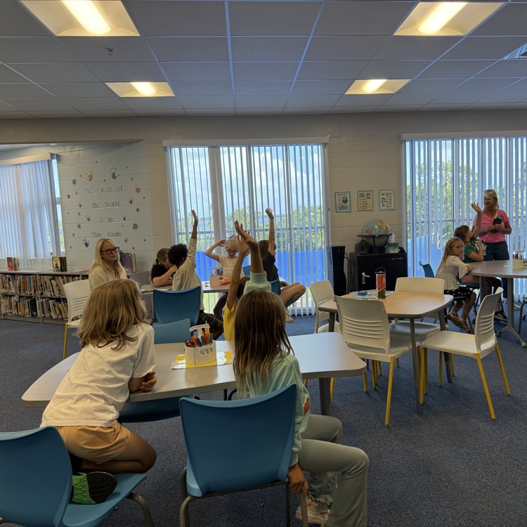 students raise their hand in the media center awaiting to be called