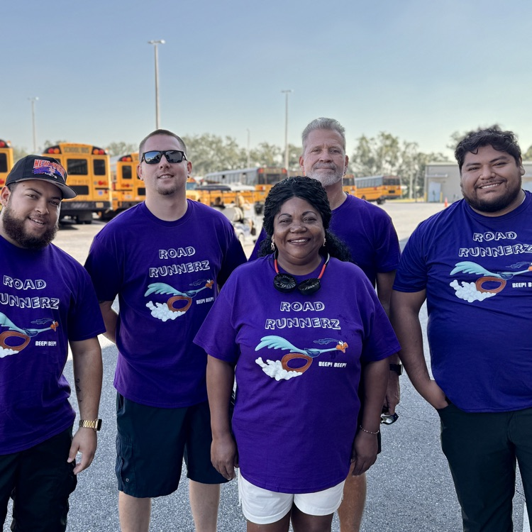 school bus drivers smile in the bus yard wearing purple shirts