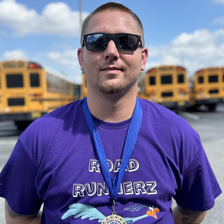 An award winning school bus driver smiling in a purple shirt and sunglasses