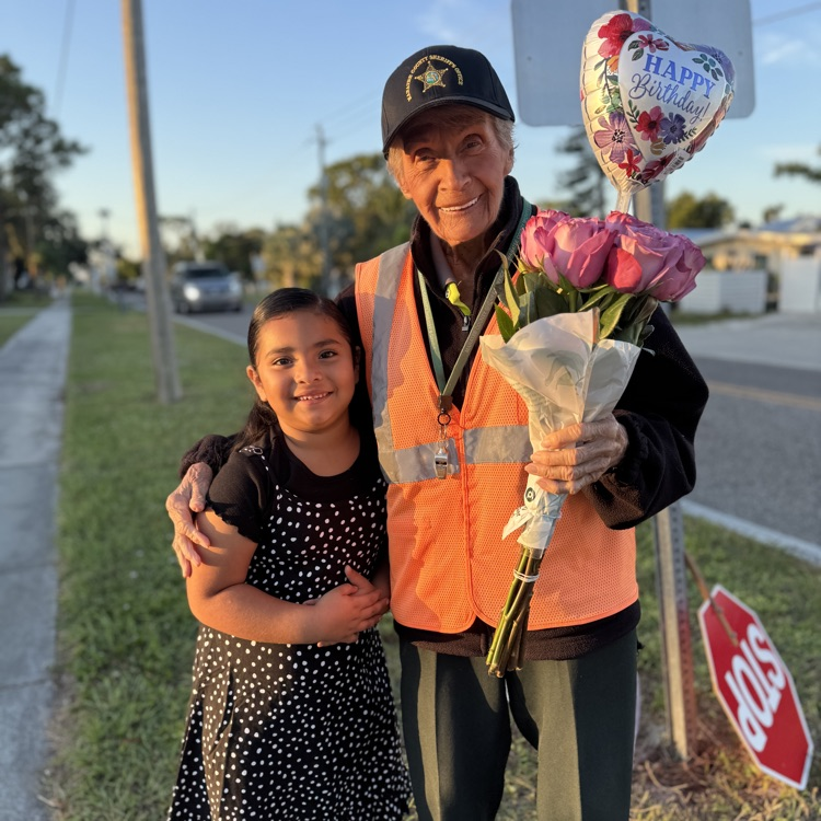 A kindergarten student stops to deliver a dozen roses and a happy birthday balloon to her school crossing guard