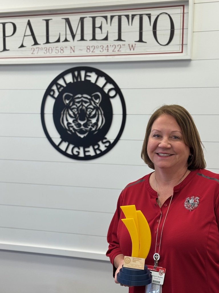 The principal holding a student-made trophy with a tiger hanging on the wall behind her.