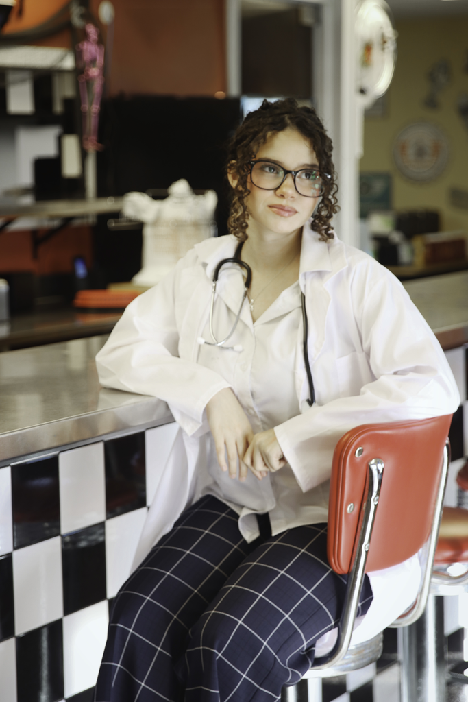 A young woman with stethoscope around her neck while sitting in a diner seat. 