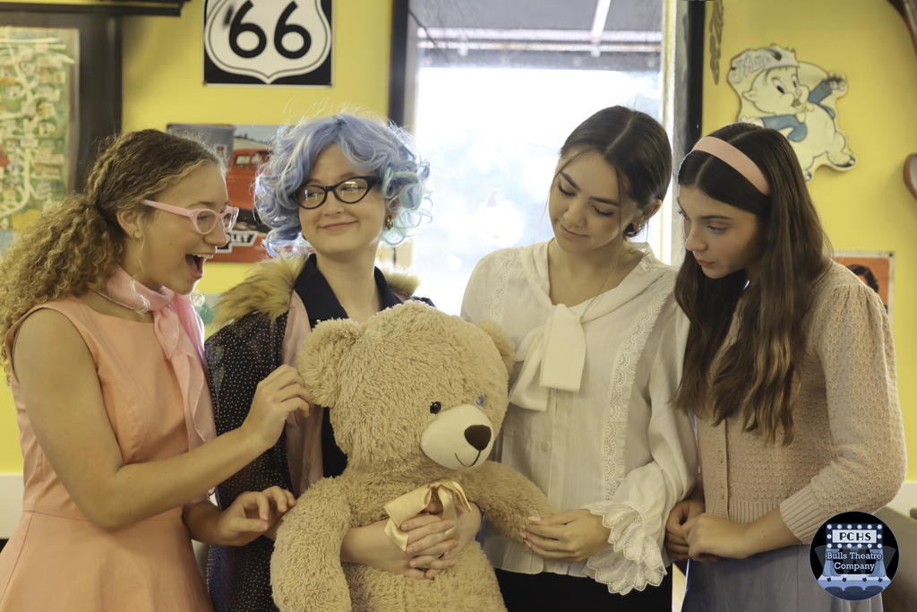 Four young girls smiling while one holds a large teddy bear.