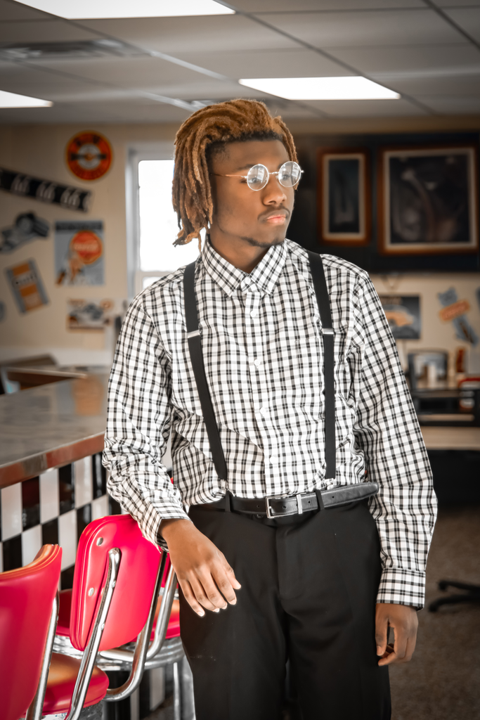 A theatre actor wearing a black and white checkered shirt and suspenders. 