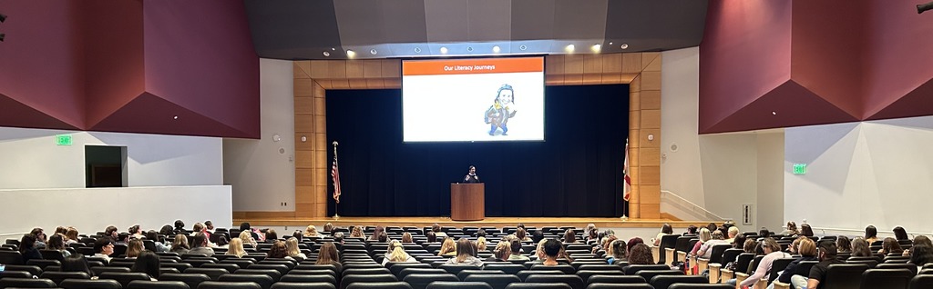 Early learning educators listen to a guest speaker in an auditorium.