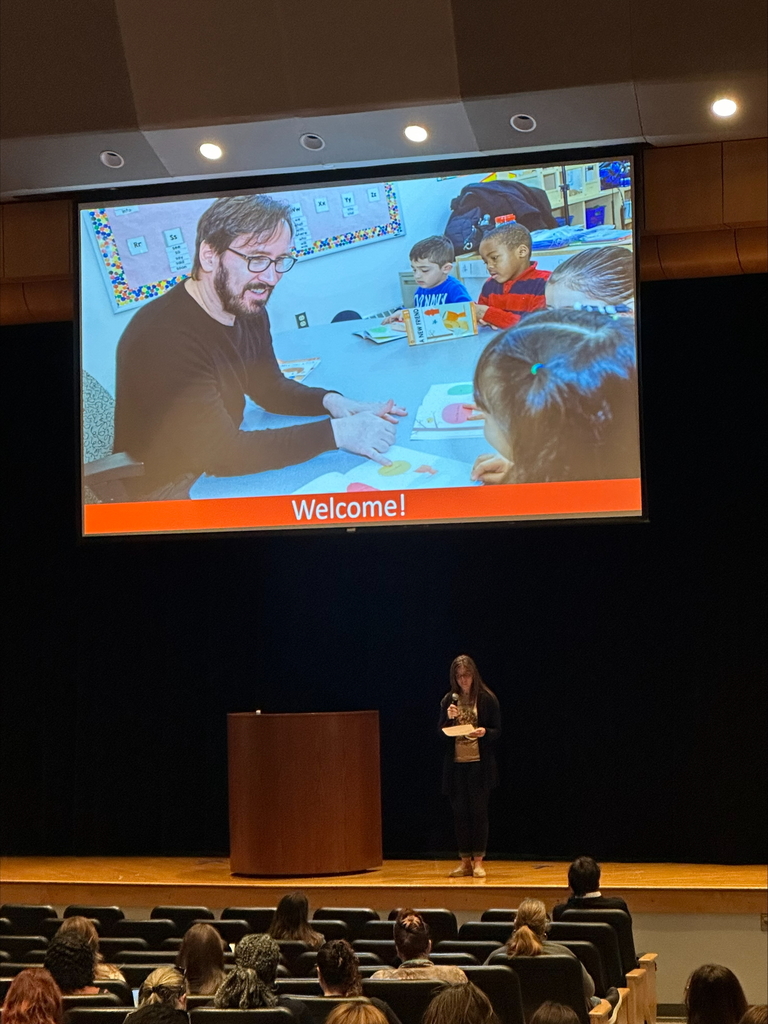 An auditorium with a screen of a special guest speaker working with children.