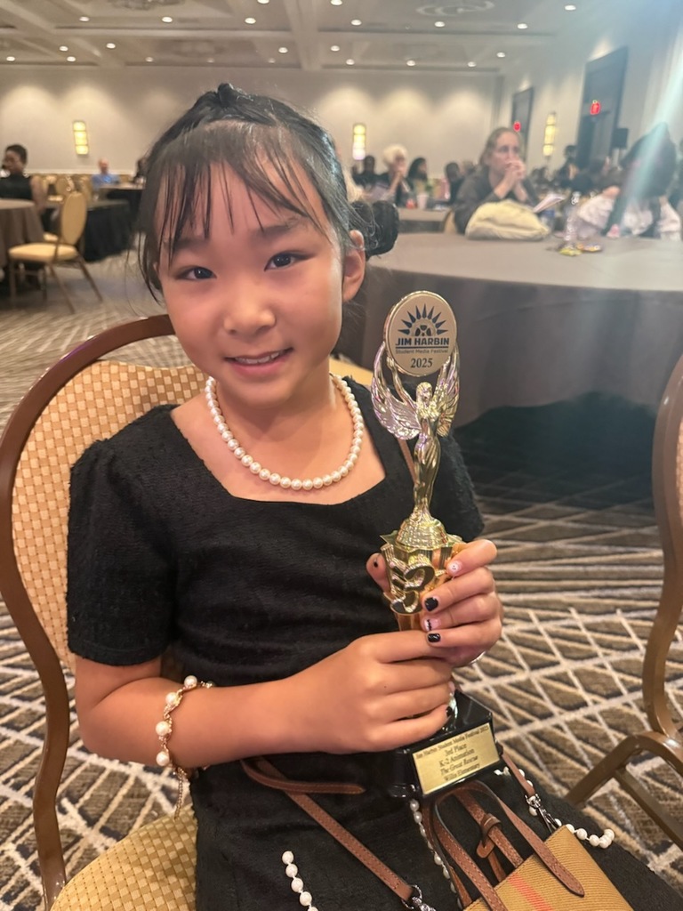 A young girl holding a trophy from a student film festival.