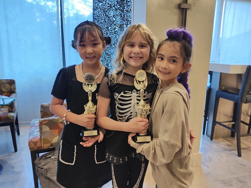 Three elementary aged filmmakers hold their winning trophies.