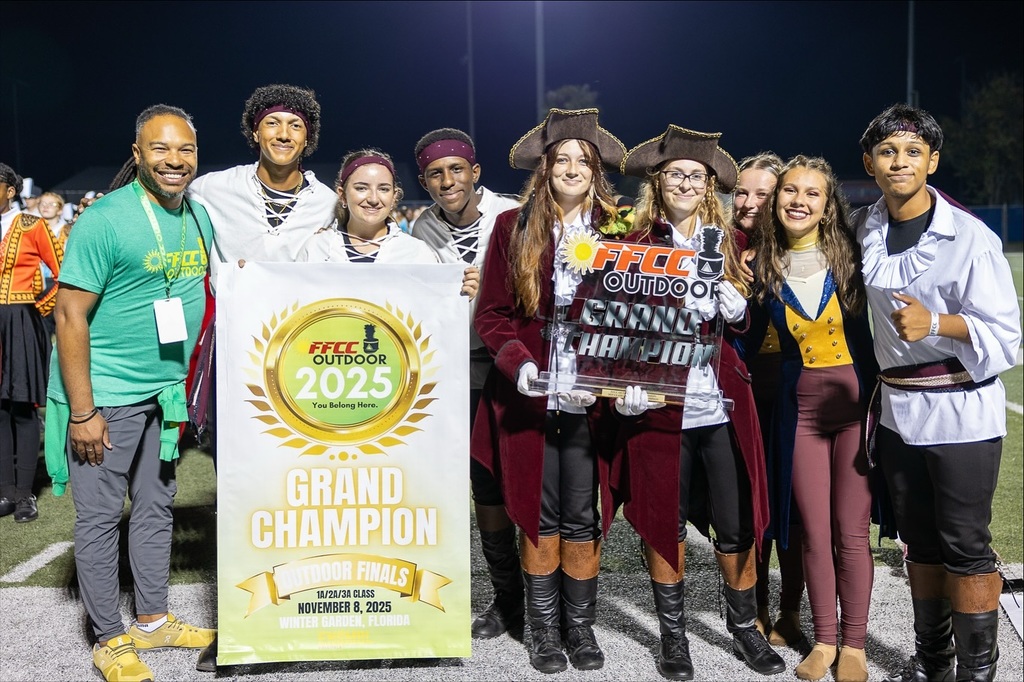 Marching band members stand shoulder to shoulder holding awards earned in a competition