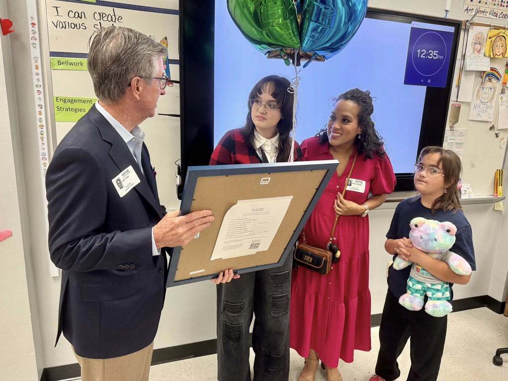 State Senator Jim Boyd holding a student artwork with her family looking on. 