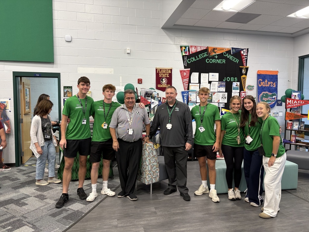A college and career advisor, school principal, and students all wearing green smile for a photo.