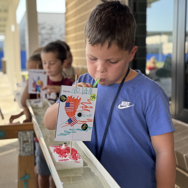 A boy blows through a straw to move his boat down a rain gutter
