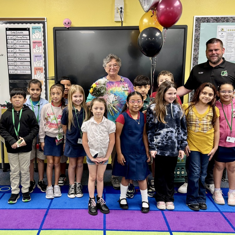 A paraprofessional, smiling with her young students surrounding her