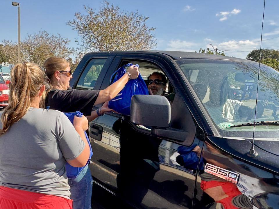 Volunteers passing out bags to a line of cars during a turkey giveaway.