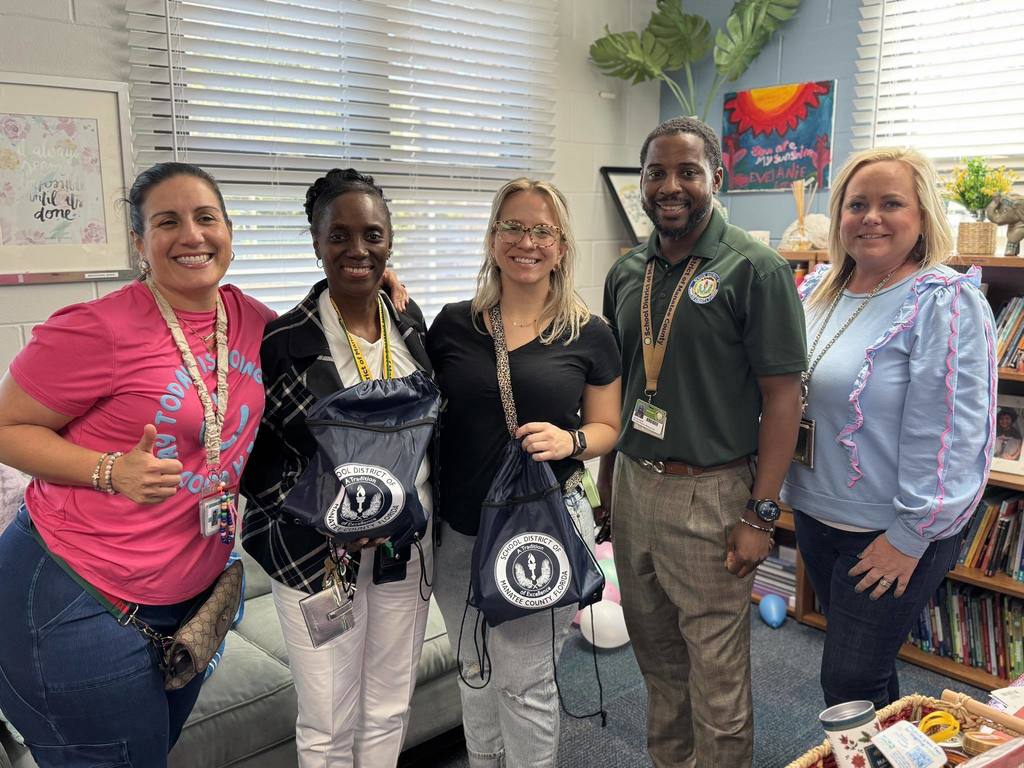 Staff and district employees smiling shoulder to shoulder in a school.