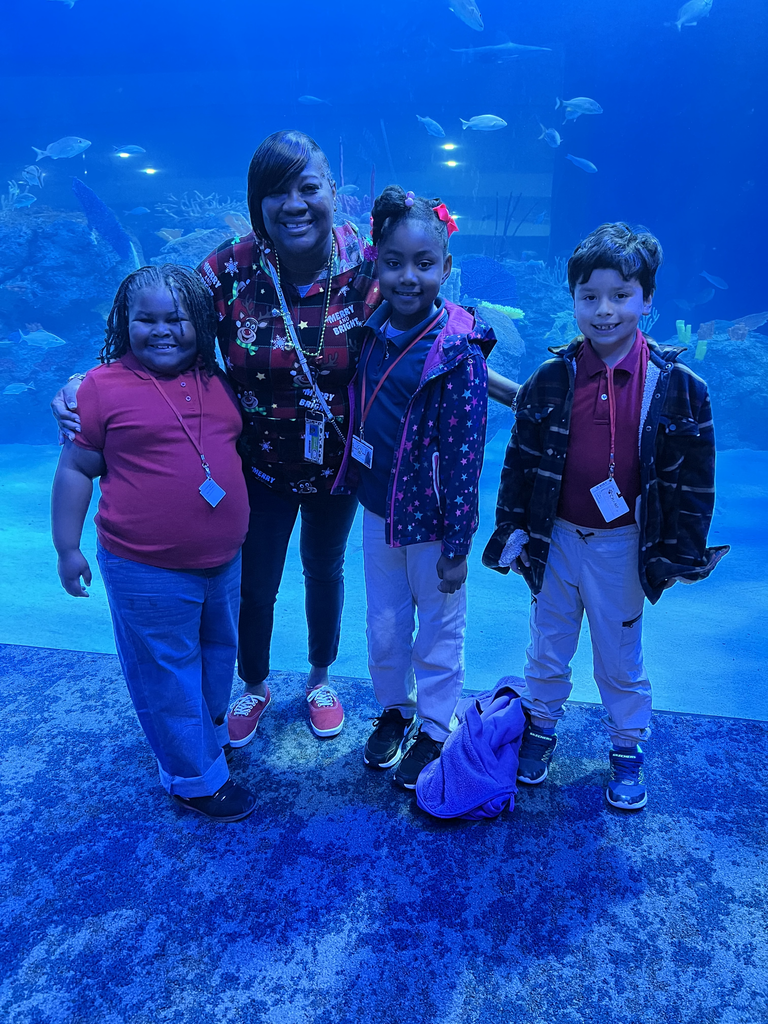 A chaperone smiles with three kids during a field trip to an aquarium.