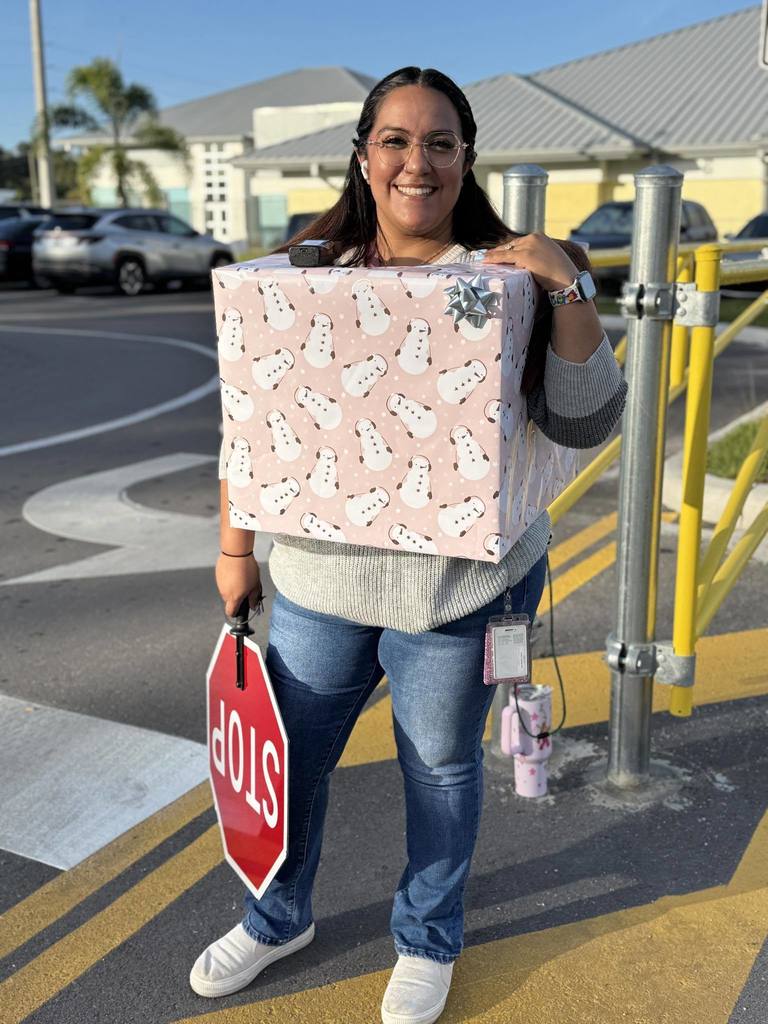 A school employee smiling and wearing a gift-wrapped box on a holiday school spirit day.